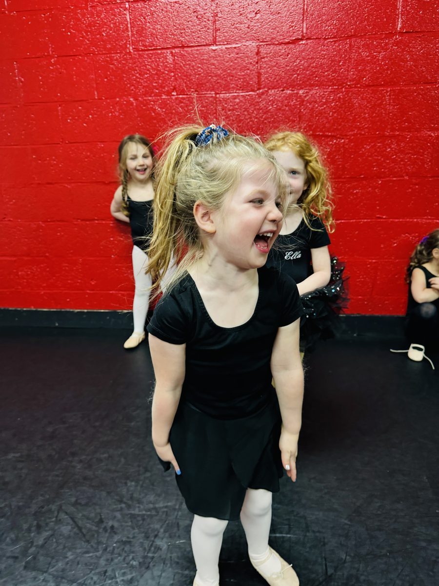 A young AFDS dancer in a black leotard laughing mid-class