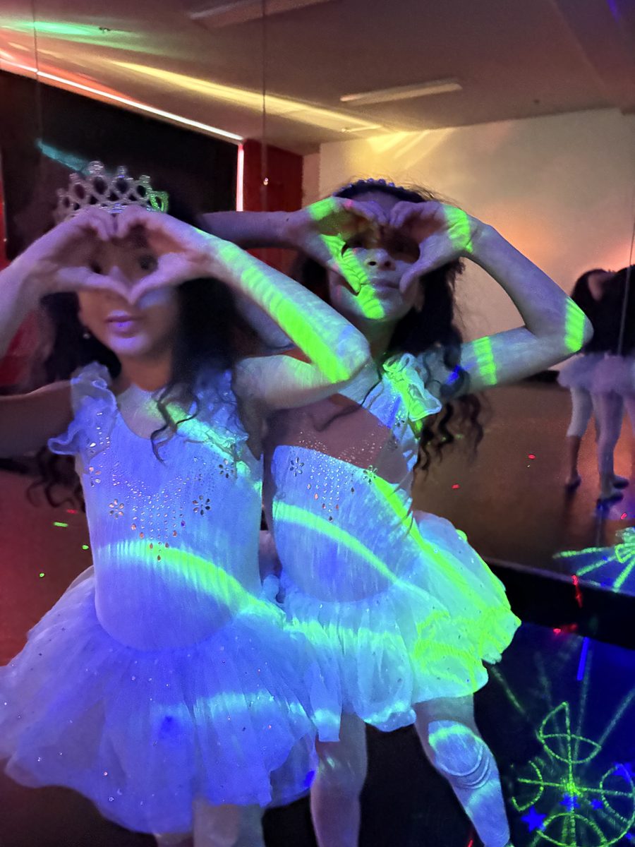 Party guests in glowing white tutus making heart hands under the black lights